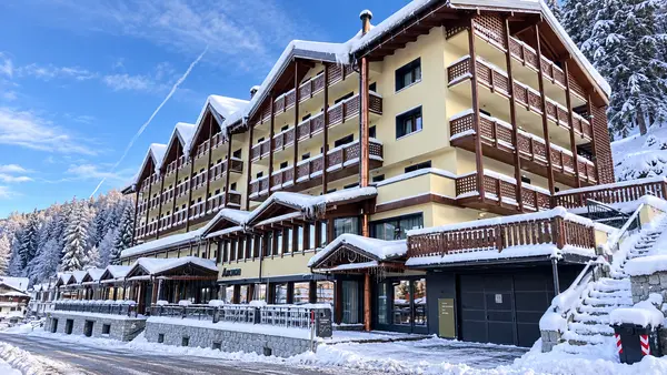 Facciata dell'Hotel Armon in stile chalet alpino innevato sotto un cielo azzurro