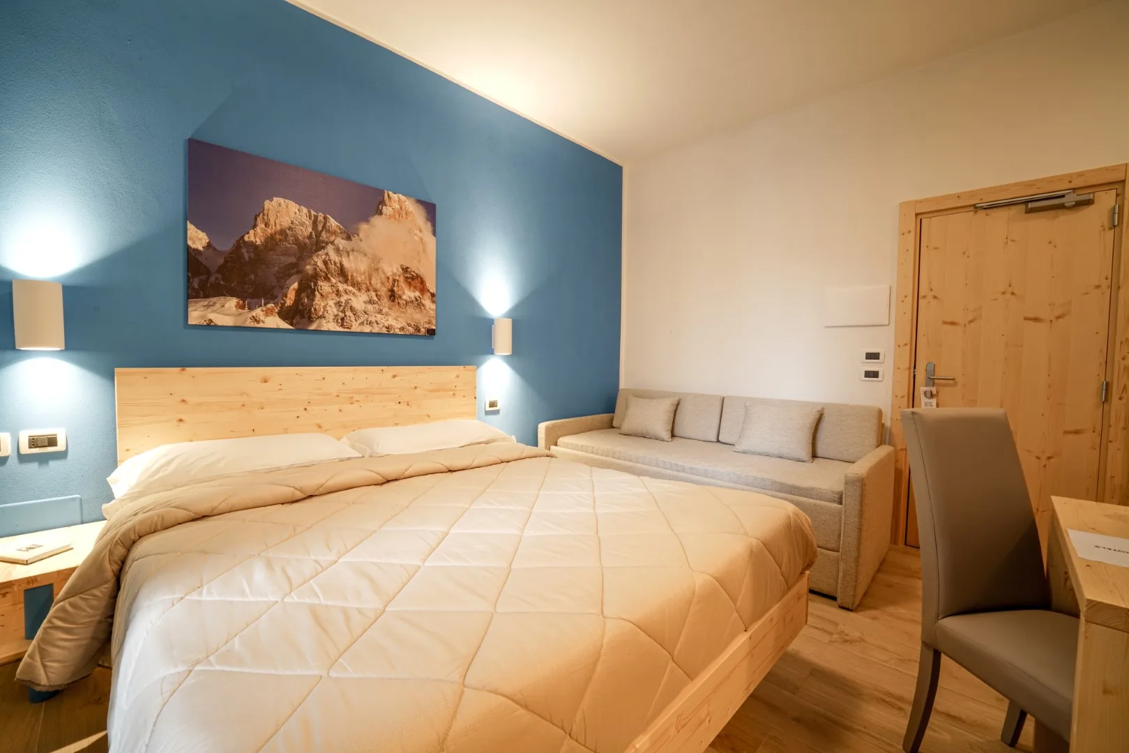 Camera luminosa con parete blu, letto in legno, divano e scrivania