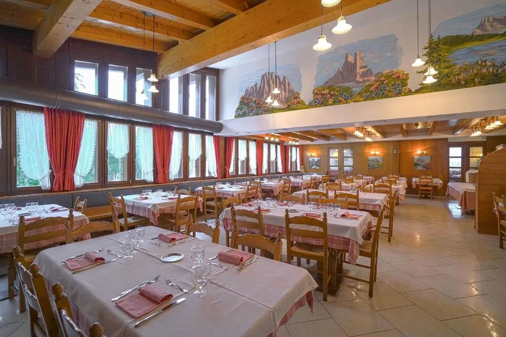 Ampia sala ristorante con tavoli apparecchiati, travi in legno e murales di montagna