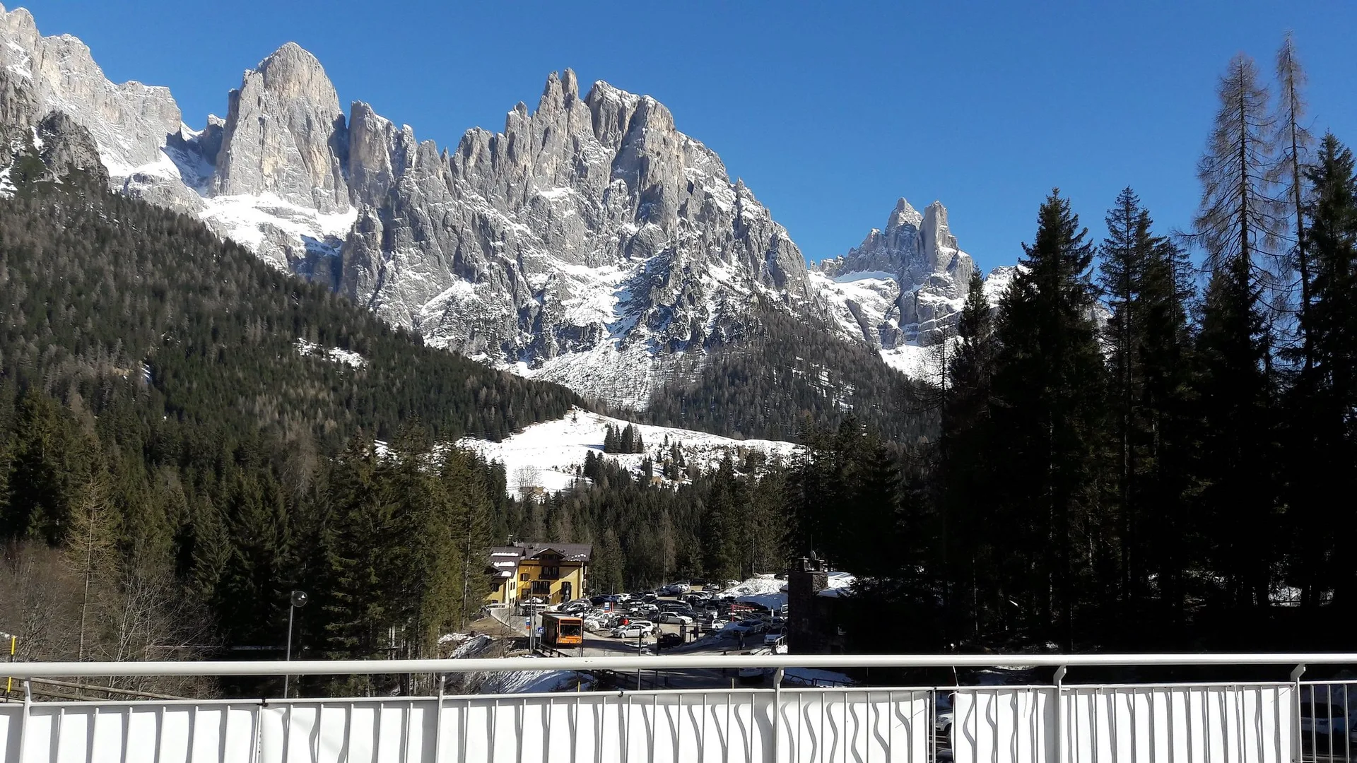 Vista dalla terrazza sulle vette dolomitiche innevate con bosco e parcheggio sottostante