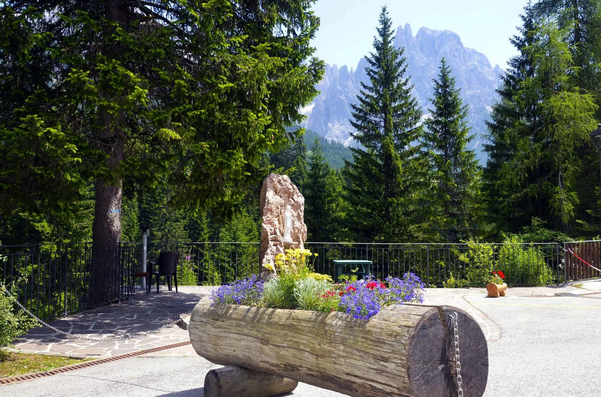Terrazza esterna estiva con fioriera in tronco di legno e vista sulle cime rocciose
