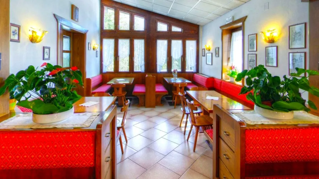 Sala da pranzo luminosa con panche rosse, tavoli in legno e piante verdi