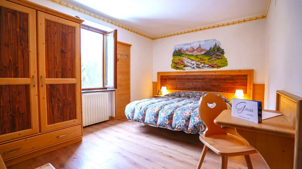 Camera con letto matrimoniale, armadio in legno e dipinto montano
