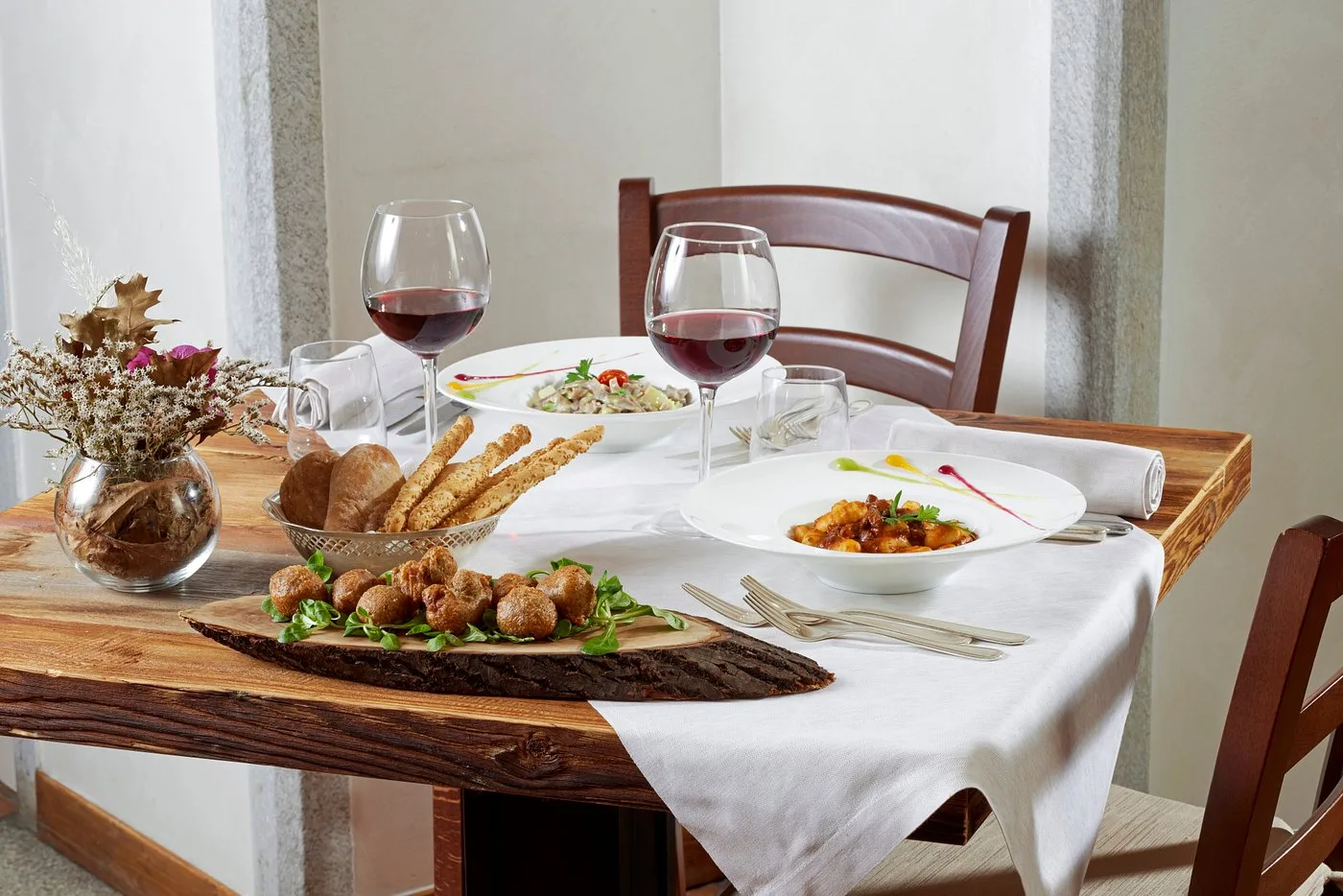 Tavolo apparecchiato con piatti gourmet, vino rosso e cestino di pane