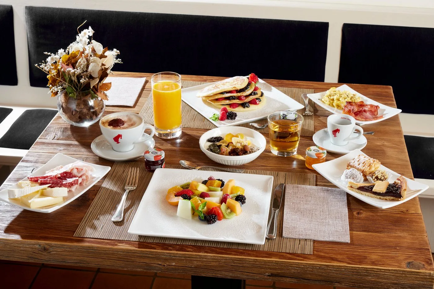 Colazione servita con frutta, pancake, cappuccino e succo d'arancia