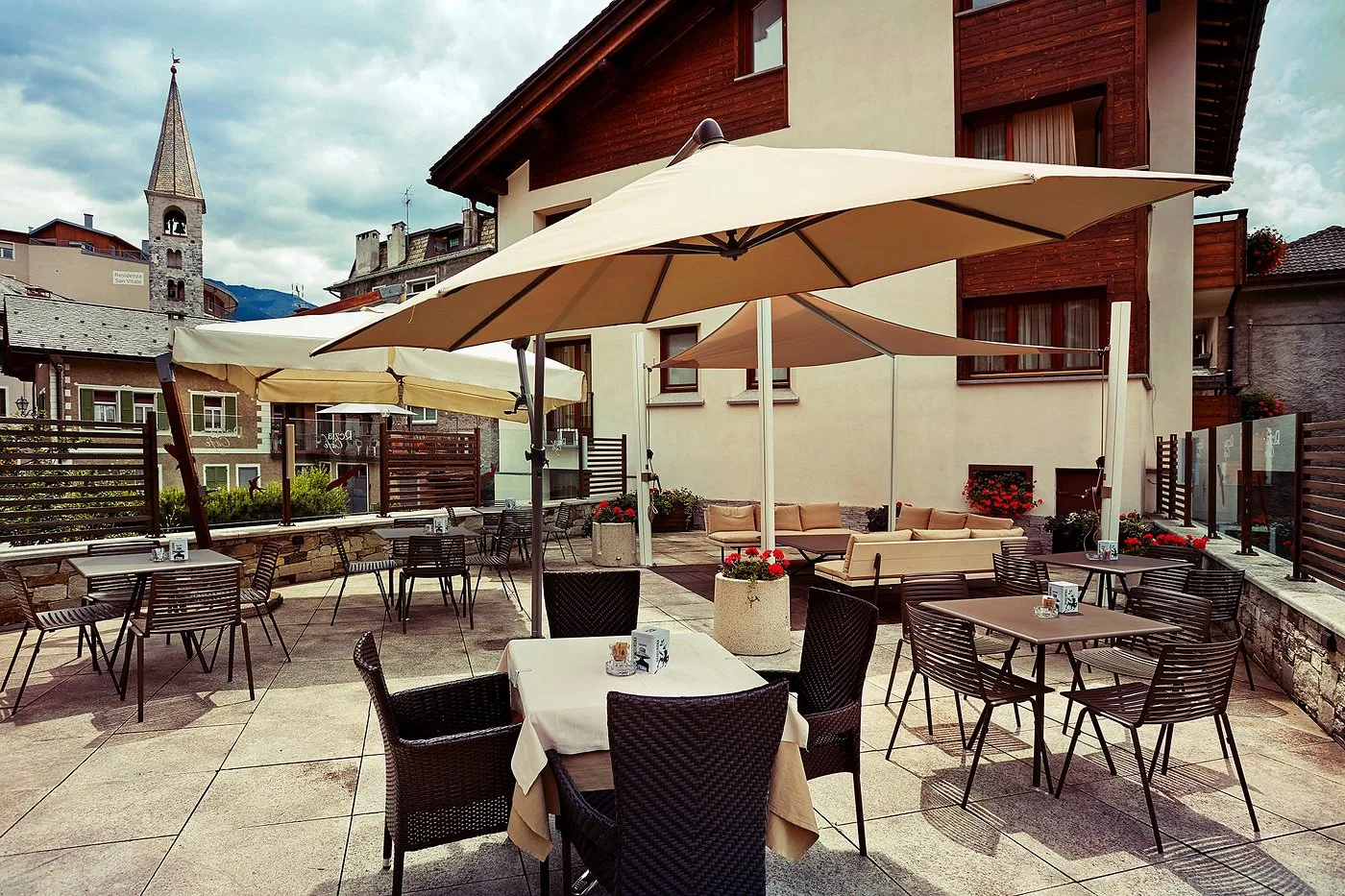 Terrazza esterna con tavoli, ombrelloni e vista sul campanile del paese