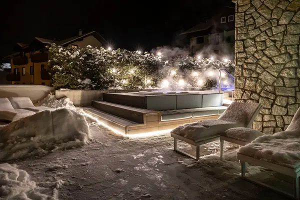 Vasca idromassaggio esterna fumante di notte con lettini innevati e illuminazione soffusa