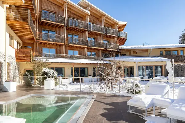 Terrazza dell'hotel in inverno con piscina esterna, lettini innevati e facciata in legno