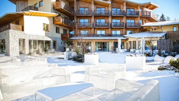 Facciata dell'hotel in legno con terrazza invernale, poltrone bianche e vapore dalla zona wellness