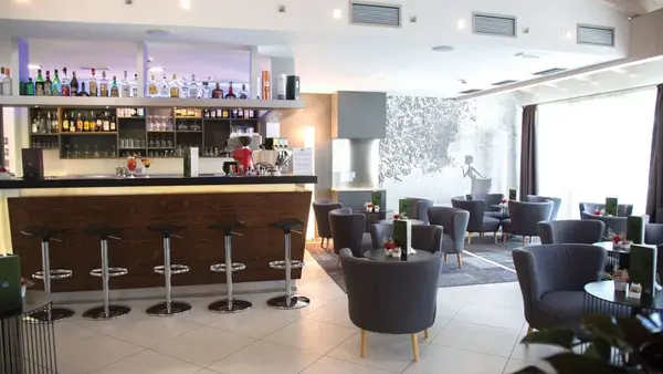 Bar interno dell'hotel con bancone in legno, sgabelli e poltrone grigie