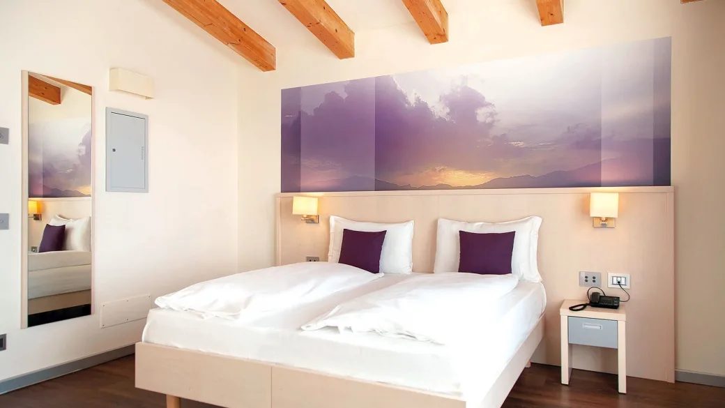 Camera matrimoniale luminosa con travi a vista e quadro panoramico sopra il letto