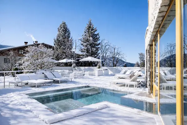 Piscina esterna riscaldata circondata da neve e abeti innevati sotto cielo azzurro