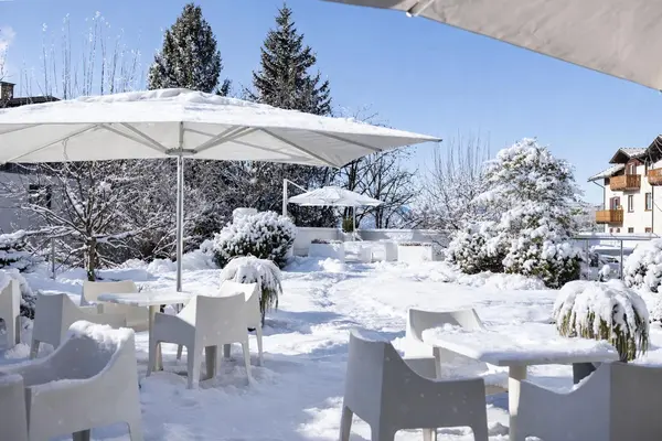 Terrazza esterna con tavoli e sedie bianche, ombrelloni e vegetazione innevata