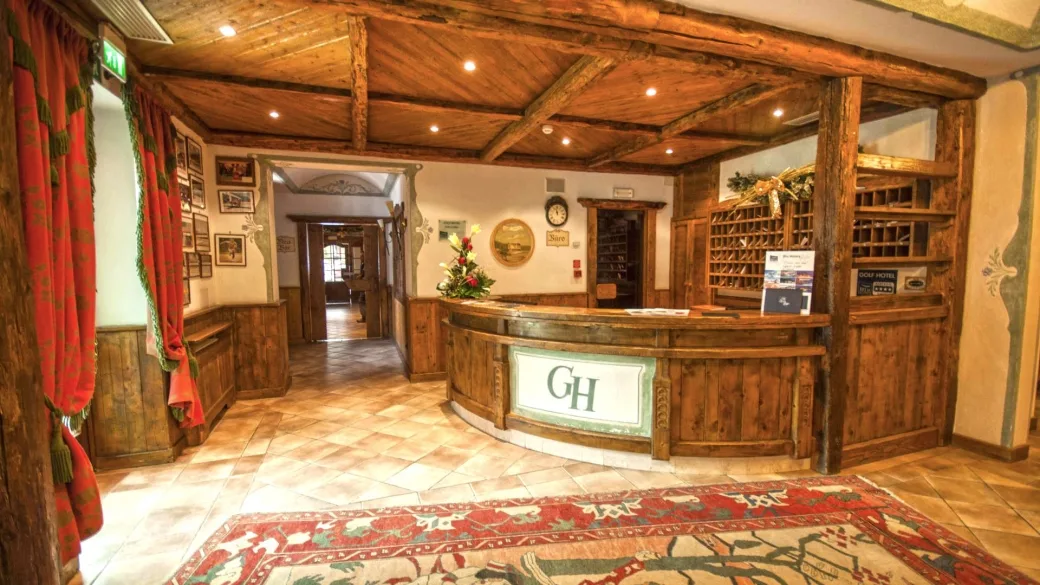 Reception del Golf Hotel con bancone in legno rustico, travi a vista e tappeto decorativo