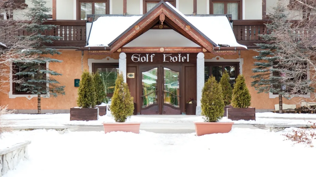 Ingresso principale del Golf Hotel con portico in legno e alberelli ornamentali nella neve