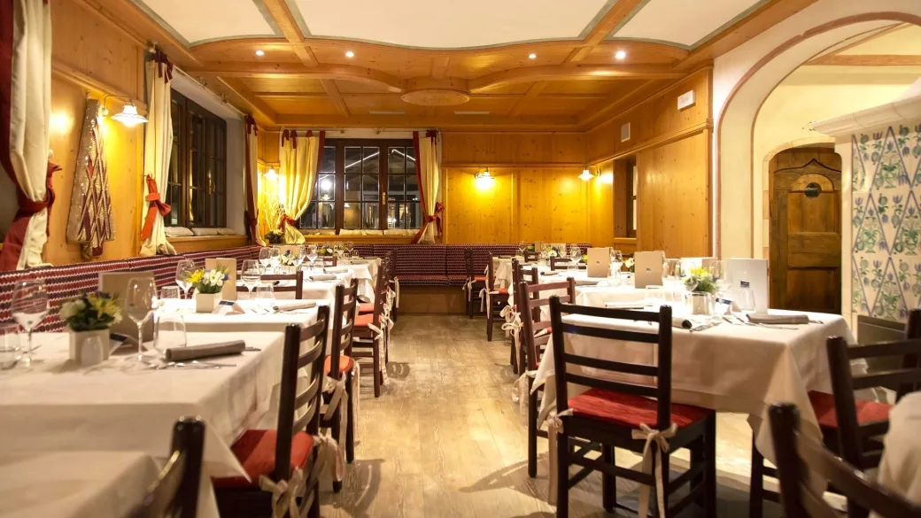 Sala ristorante in stile alpino con tavoli apparecchiati, boiserie in legno e illuminazione calda