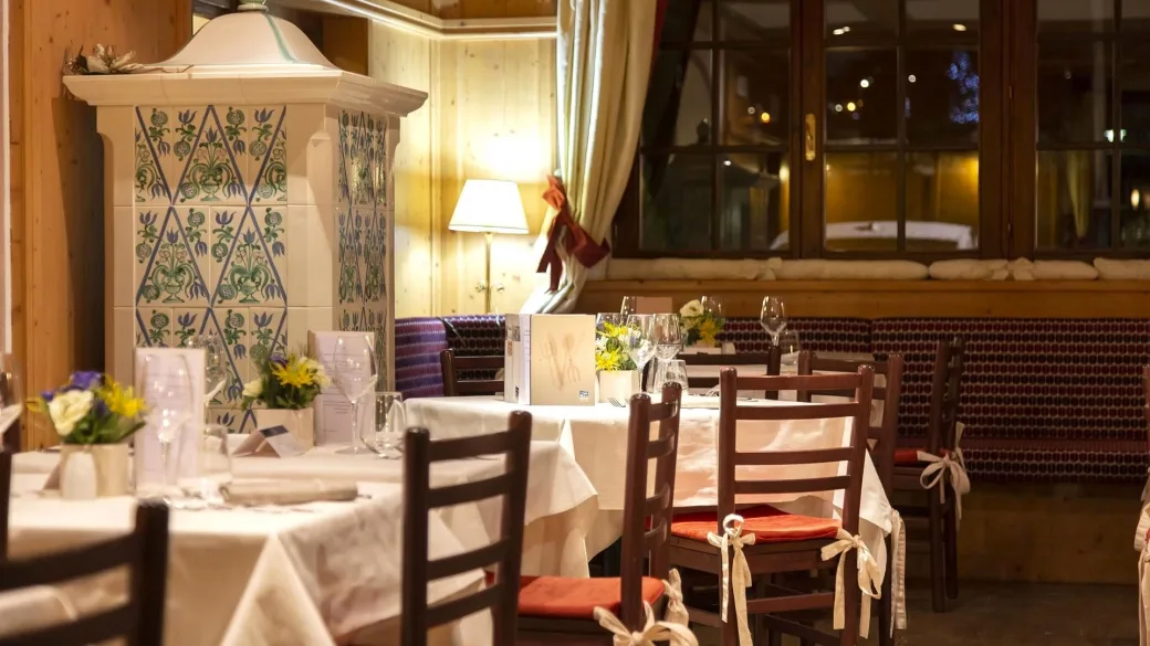 Dettaglio della sala ristorante con stufa in maiolica decorata e tavoli eleganti apparecchiati