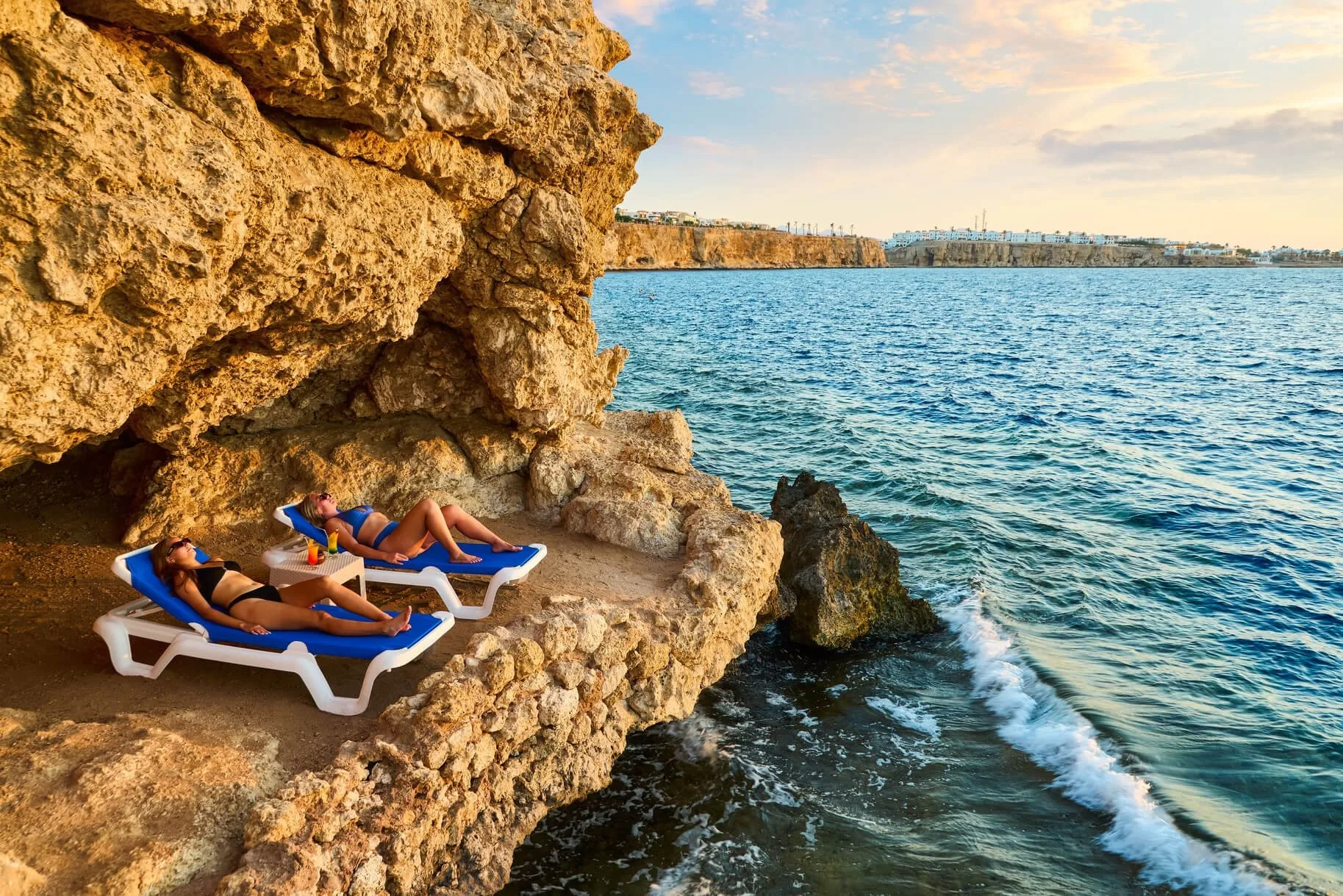Due persone prendono il sole su lettini in una nicchia rocciosa vicino al mare