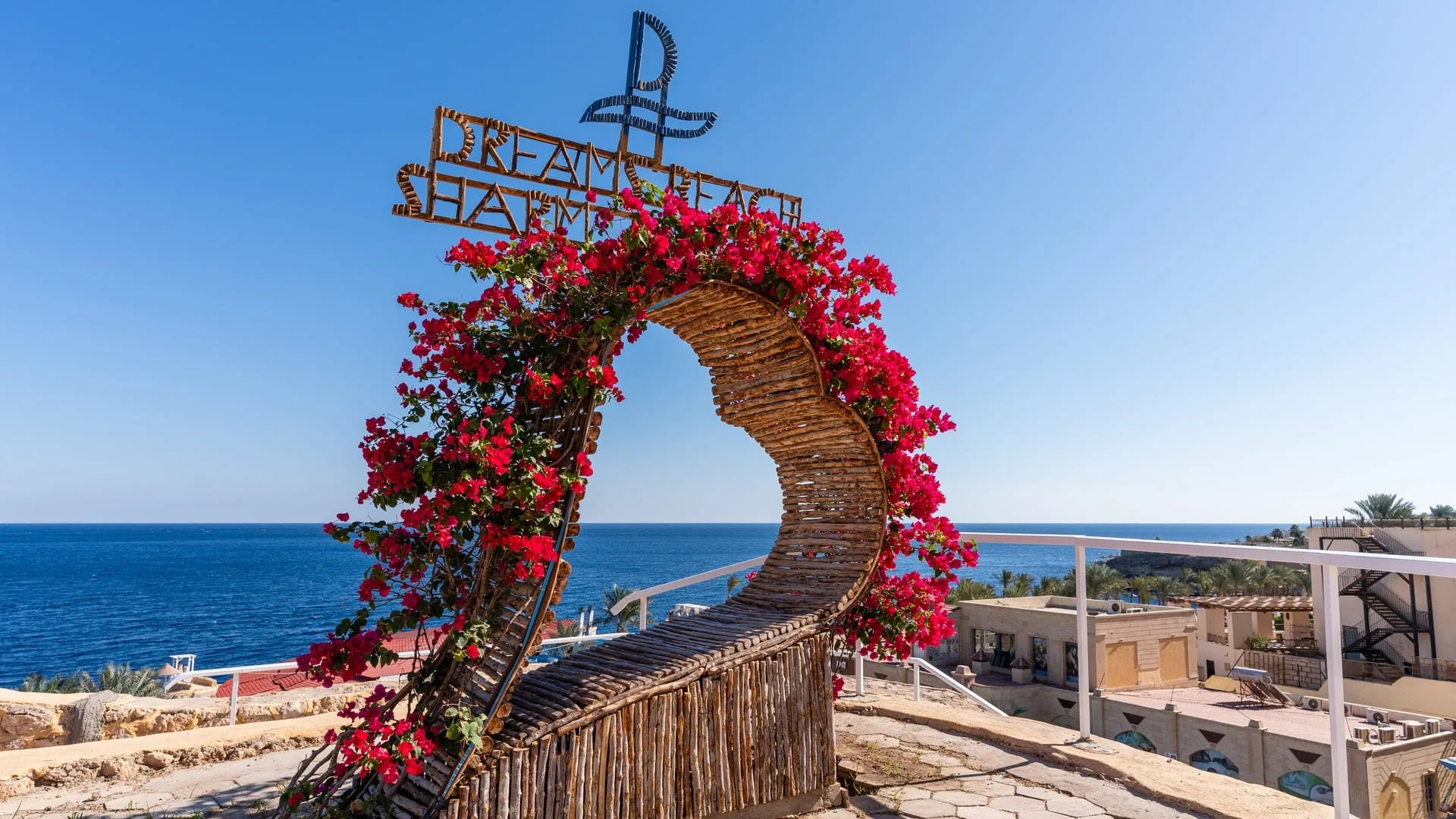 Arco decorativo in legno con fiori rossi e insegna Dream Beach affacciato sul mare