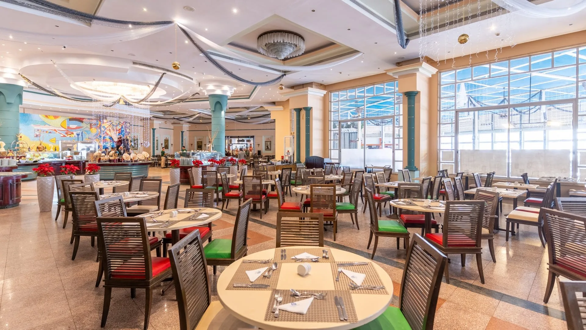 Ampia sala da pranzo con tavoli rotondi apparecchiati e buffet illuminato