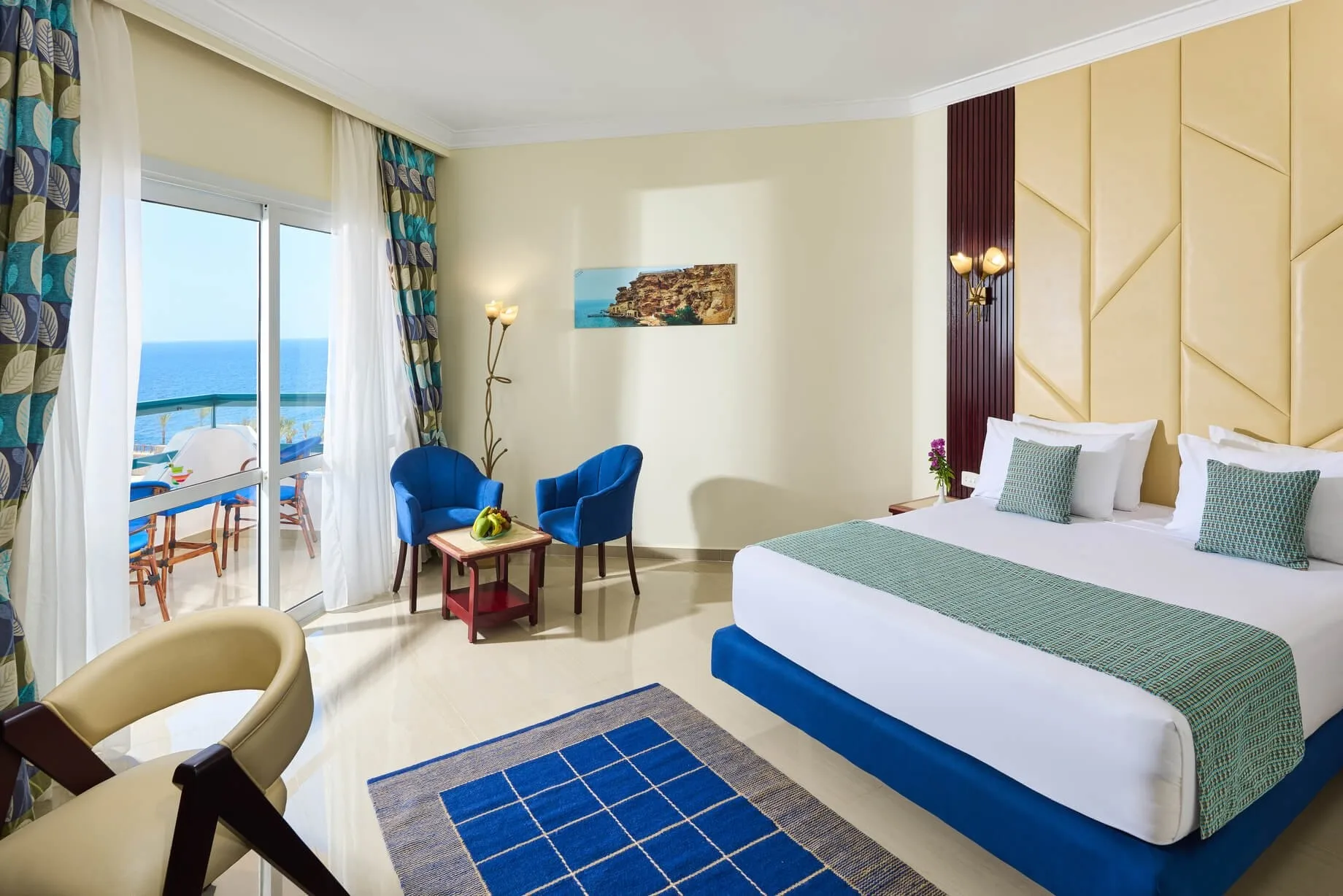 Camera elegante con letto matrimoniale, poltrone blu e balcone con vista mare