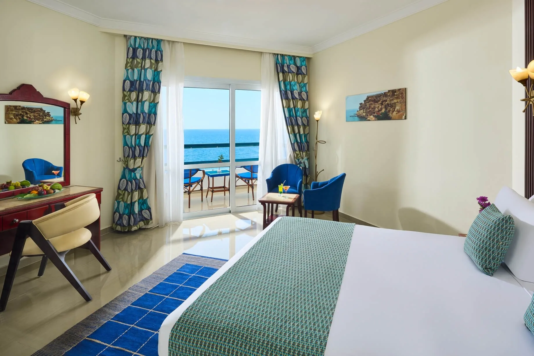Camera con letto matrimoniale, scrivania, poltrone blu e balcone con vista mare