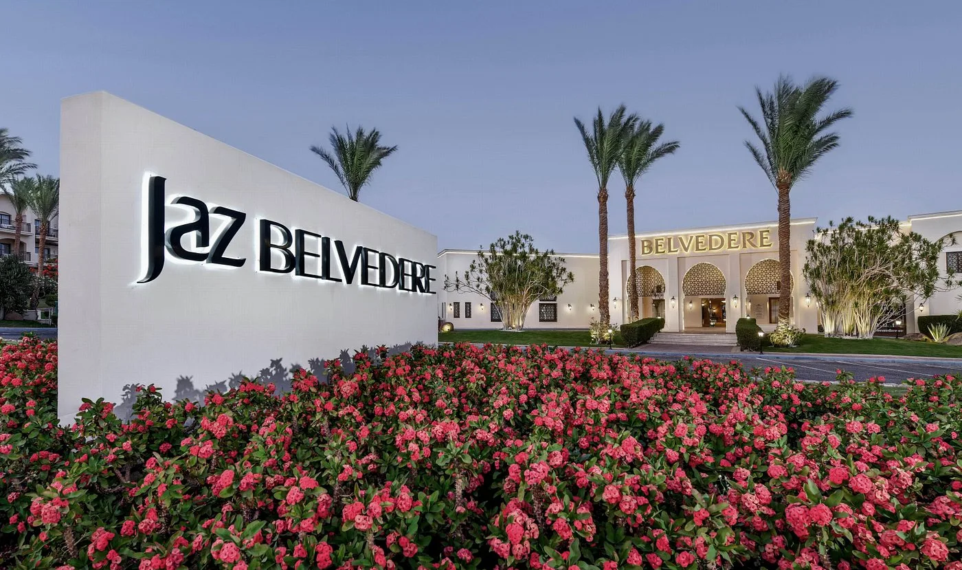 Ingresso del Jaz Belvedere con insegna, palme e aiuola di fiori rossi al crepuscolo