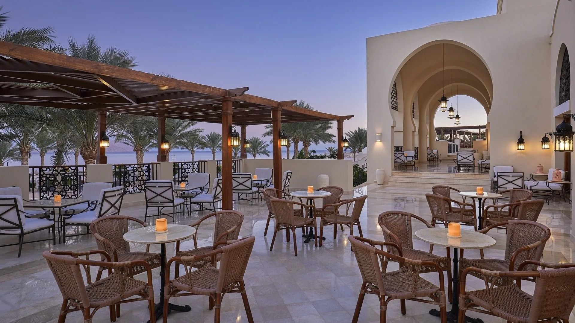 Terrazza ristorante con tavoli, sedie in vimini, pergolato e vista mare al tramonto
