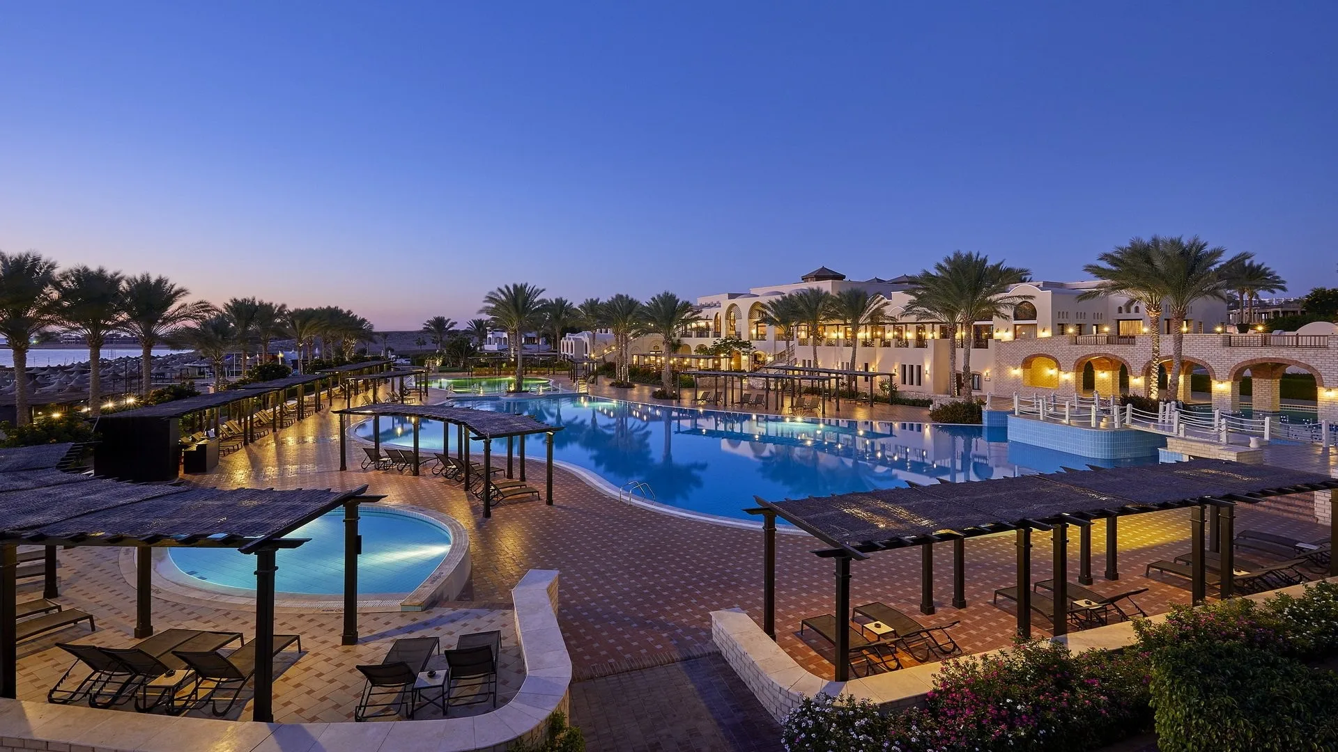Piscine del resort illuminate al crepuscolo con pergolati, lettini ed edifici in stile arabo