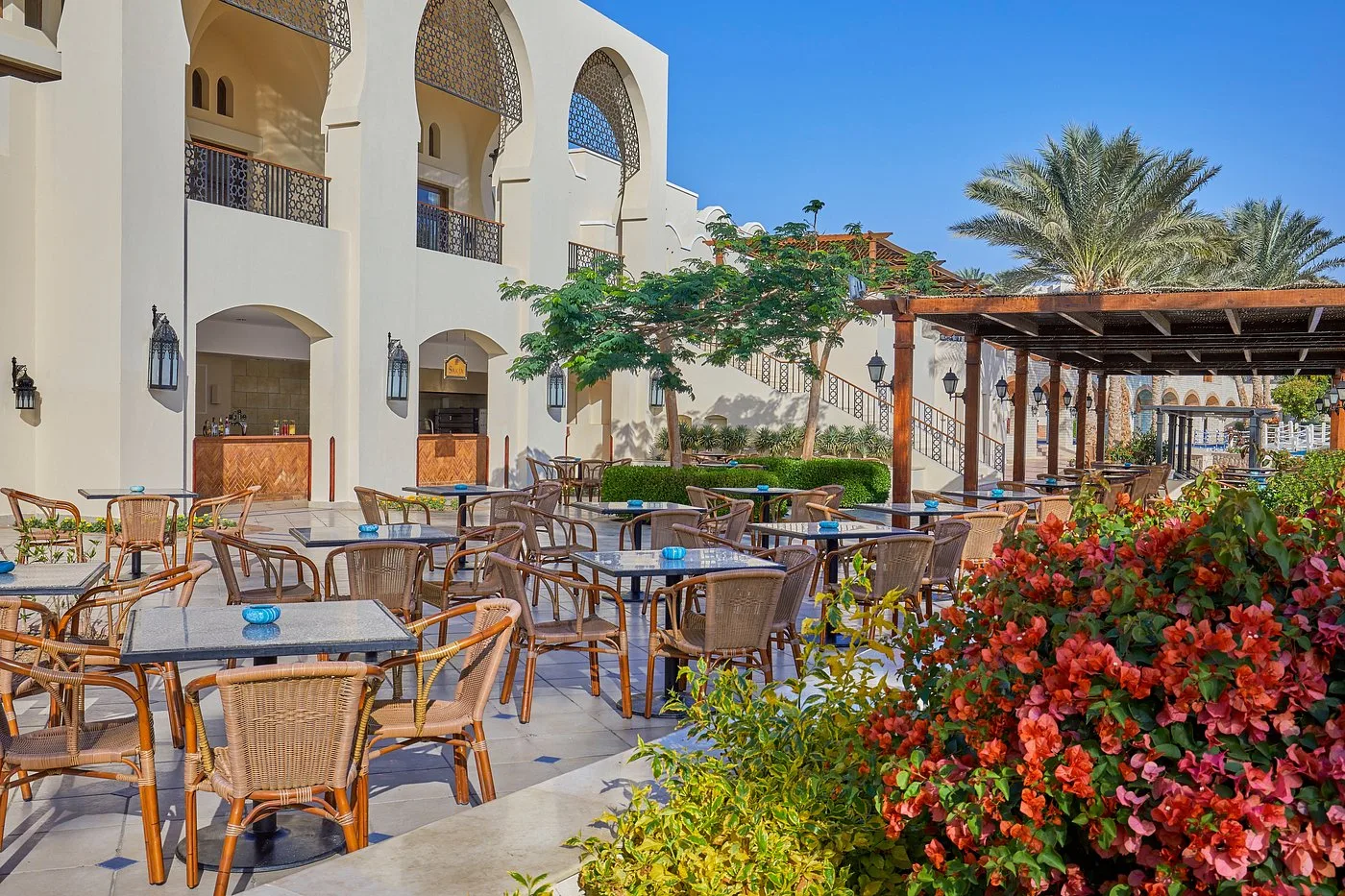 Terrazza esterna del ristorante con tavoli, sedie in vimini e bougainvillea fiorita