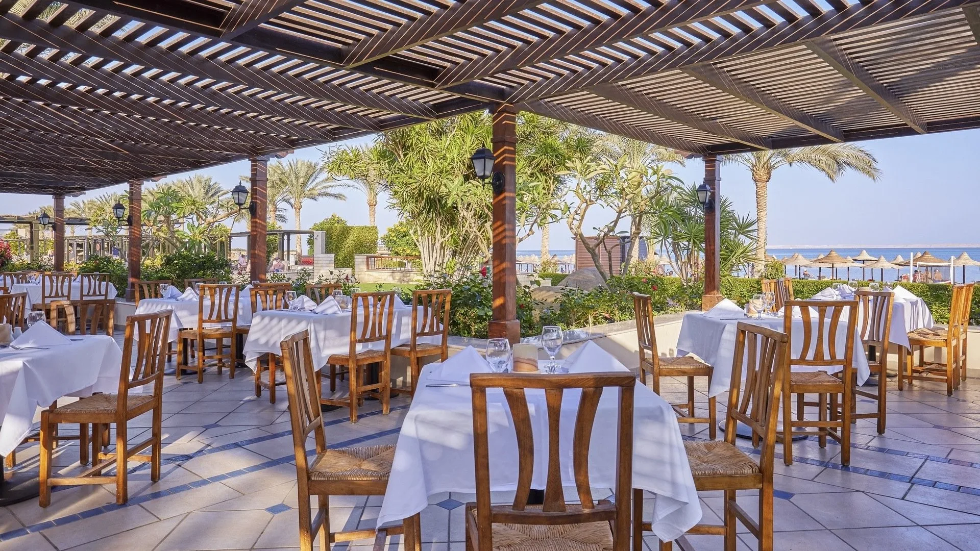 Terrazza ristorante coperta da pergolato in legno con tavoli bianchi e vista mare