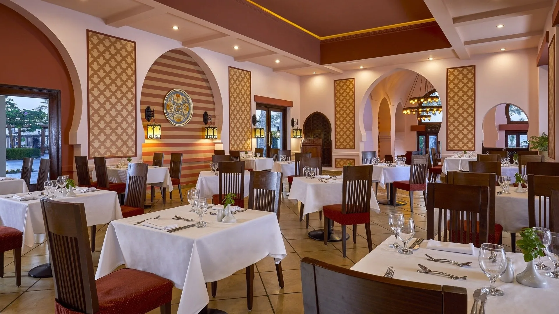 Sala ristorante interna in stile arabeggiante con archi, tavoli bianchi e sedie in legno