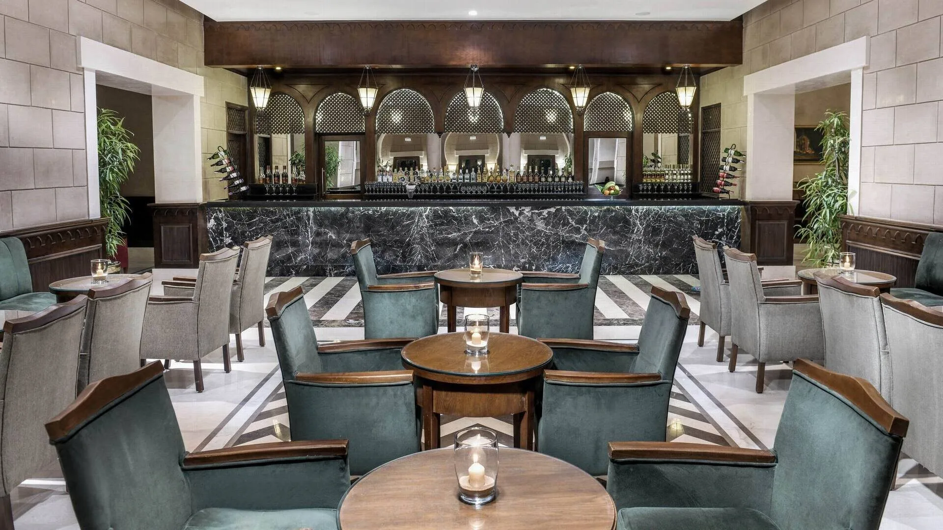 Bar interno con bancone in marmo nero, poltrone in velluto verde e tavolini in legno