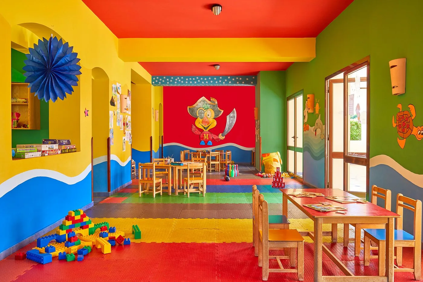 Sala giochi per bambini colorata con tavolini in legno, mattoncini e decorazioni a tema pirata