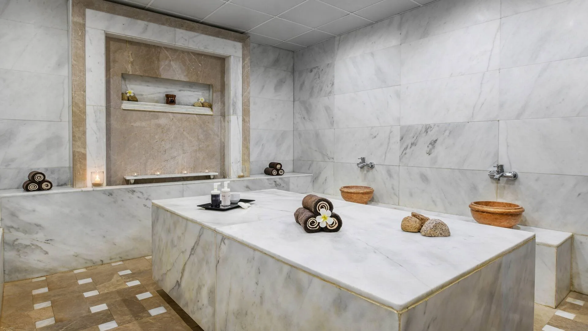 Bagno turco in marmo con panca centrale, asciugamani arrotolati e ciotole in terracotta