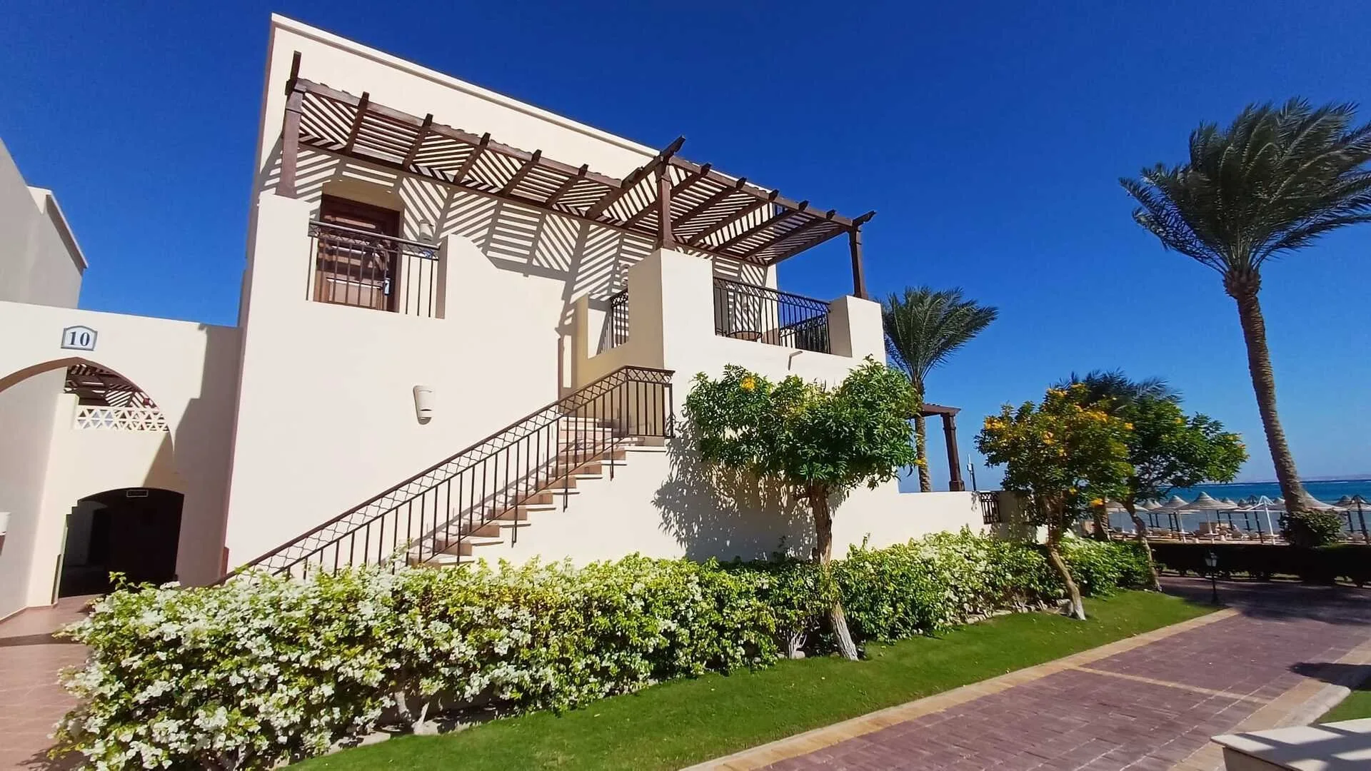 Villa bianca in stile mediterraneo con scala esterna, pergolato in legno e giardino fronte mare