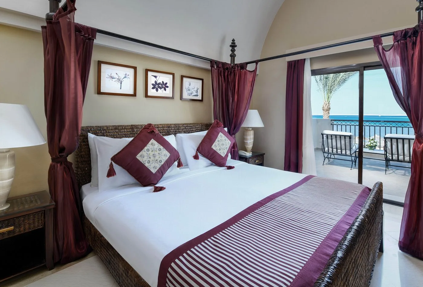 Camera con letto a baldacchino, testiera in rattan, cuscini bordeaux e balcone vista mare