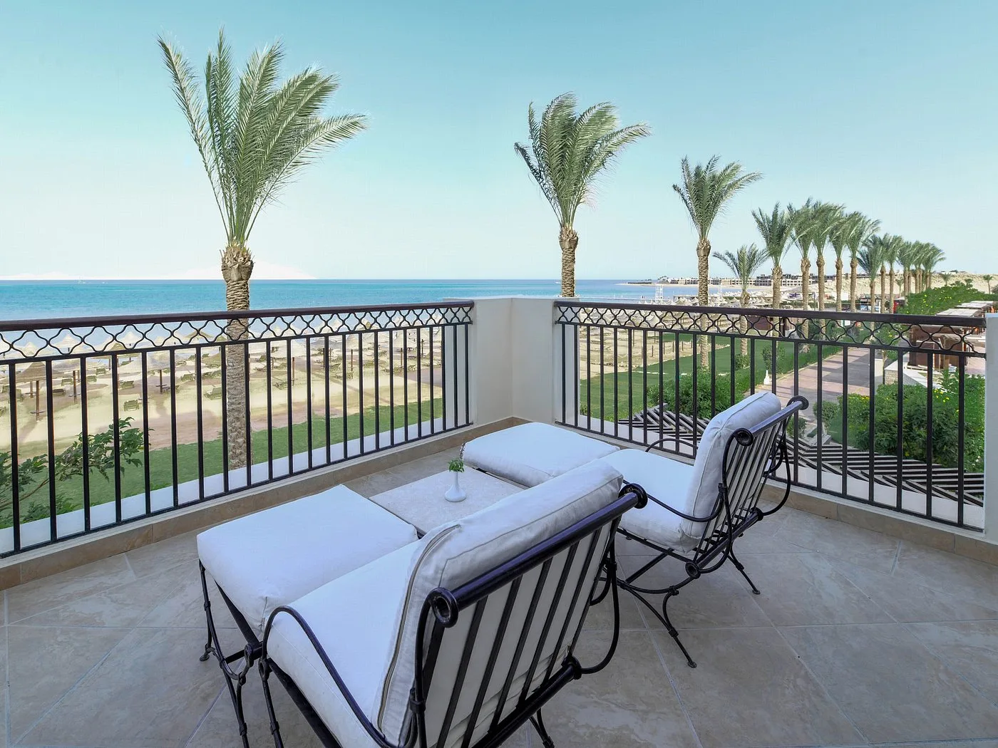Terrazza con lettini imbottiti bianchi, vista sul mare, palme e spiaggia