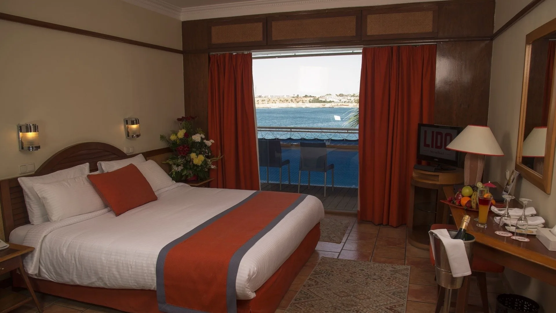 Camera elegante con letto matrimoniale, scrivania e balcone con vista mare e tende arancioni