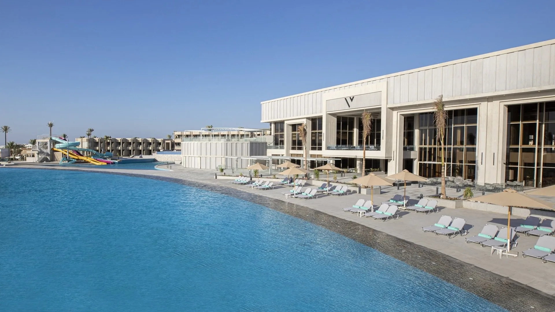 Piscina laguna con lettini e ombrelloni accanto a edificio moderno del resort con scivoli acquatici