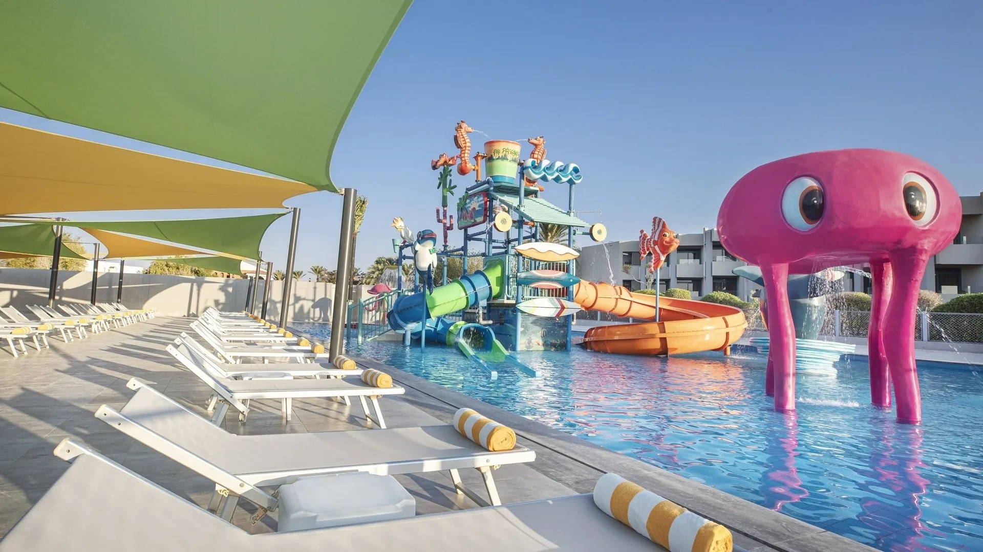 Parco acquatico per bambini con polpo rosa, scivoli colorati e lettini con teli a righe