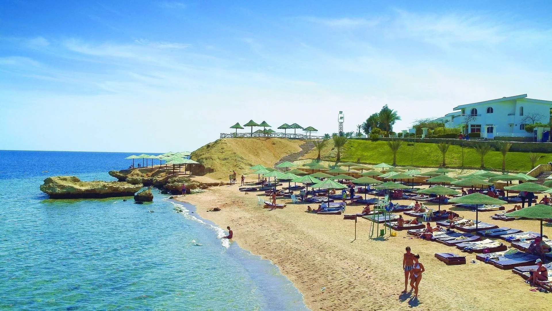 Spiaggia con ombrelloni di paglia e lettini sul mare limpido con scogliera