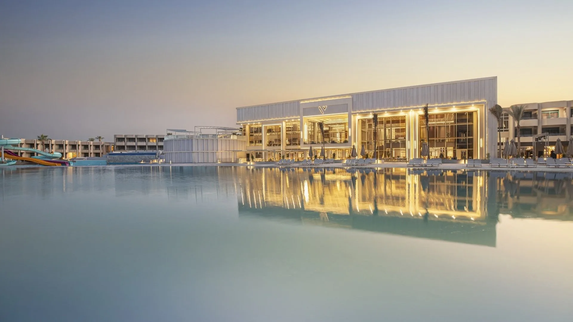 Esterno moderno del resort illuminato con piscina a sfioro e scivoli acquatici al crepuscolo