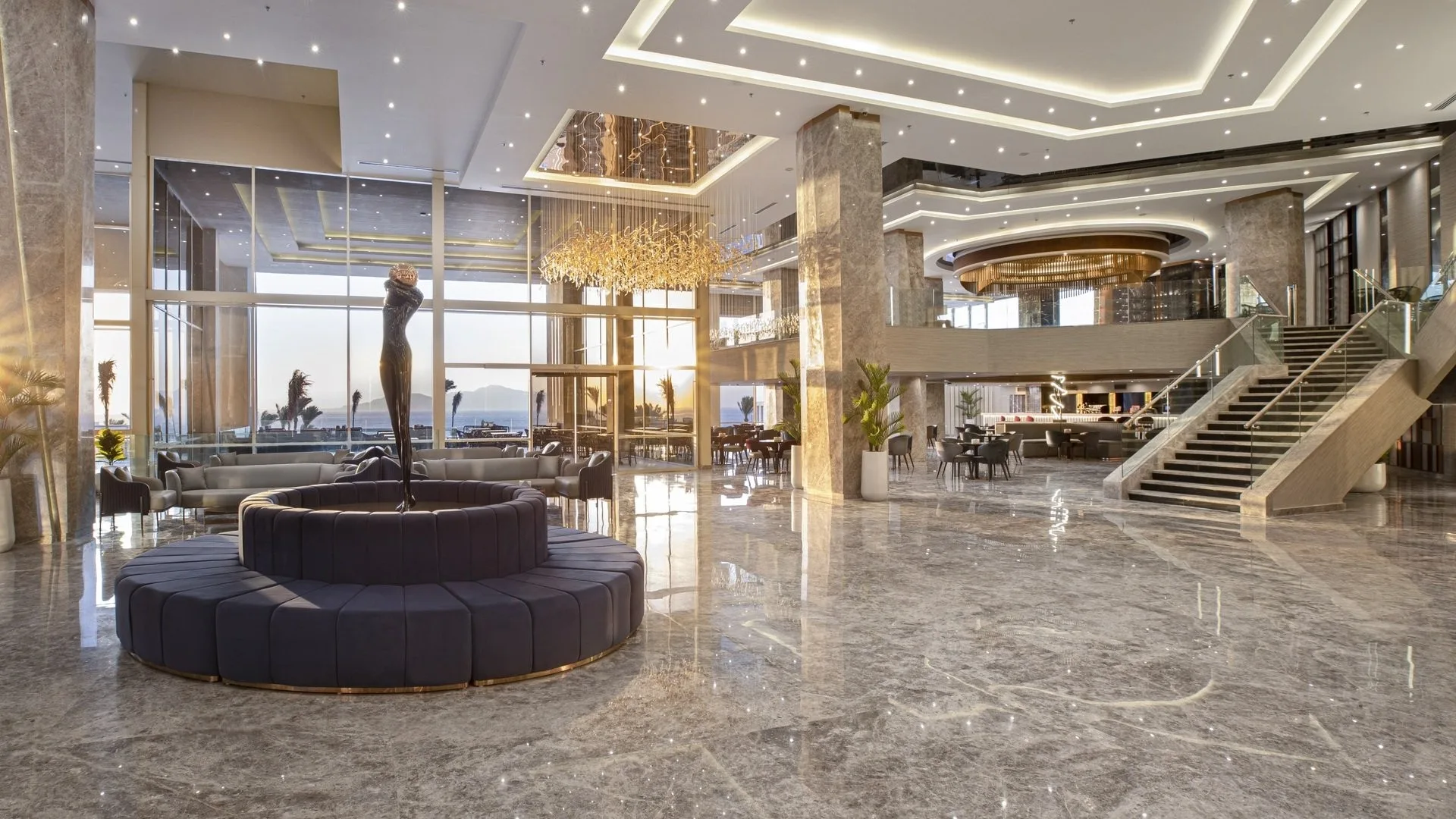 Lobby lussuosa con lampadario dorato, scultura centrale e scalinata in marmo