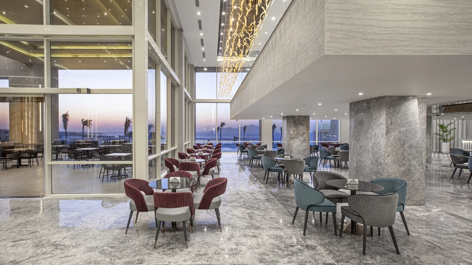 Area lounge con poltrone colorate, tavolini e vetrate affacciate sul mare al tramonto