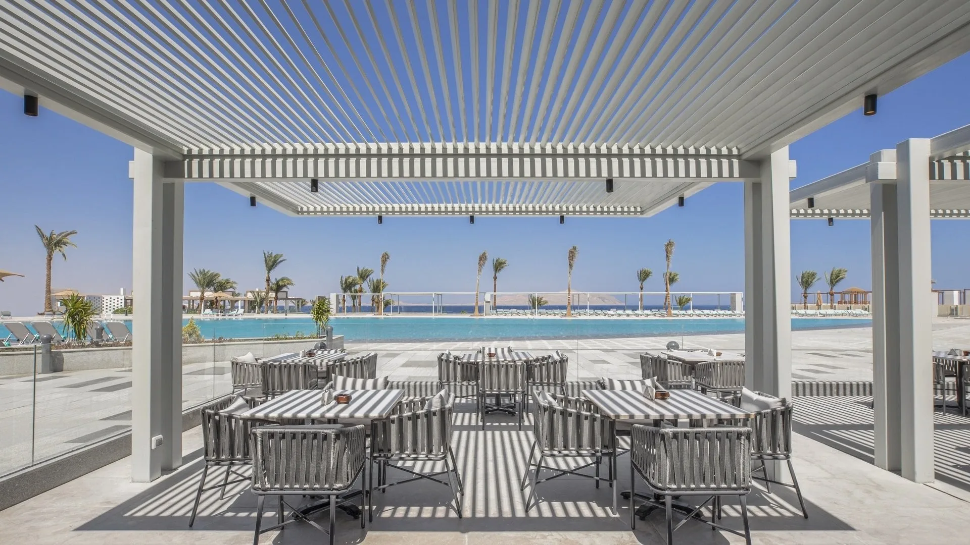 Terrazza ristorante con pergolato bianco e tavoli a righe affacciati sulla piscina e sul mare