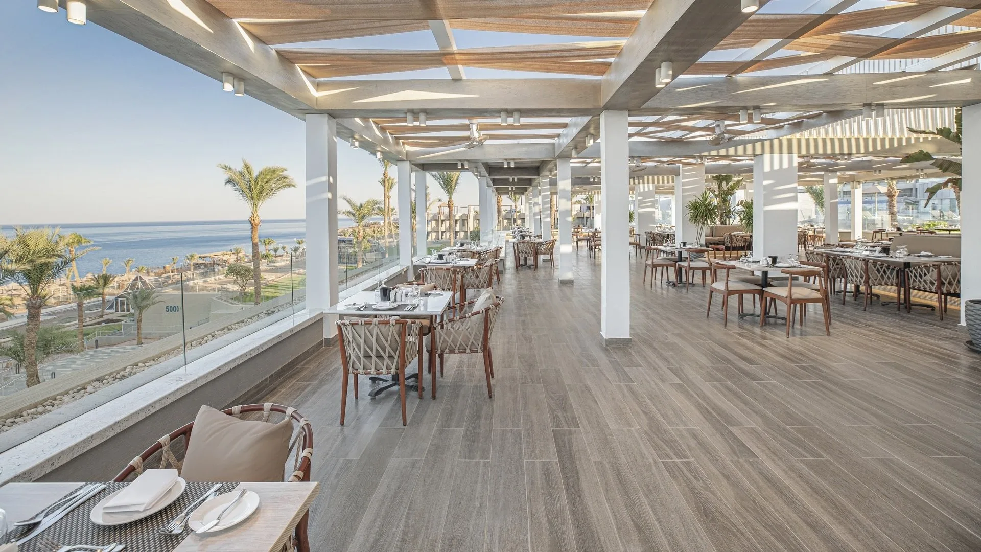 Ristorante panoramico con pavimento in legno e grandi vetrate affacciate sul mare e sulle palme