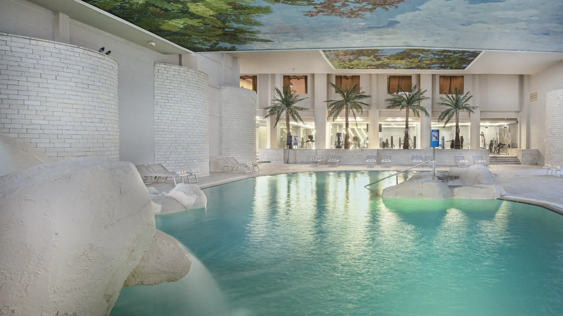 Piscina interna con rocce artificiali, palme e soffitto decorato