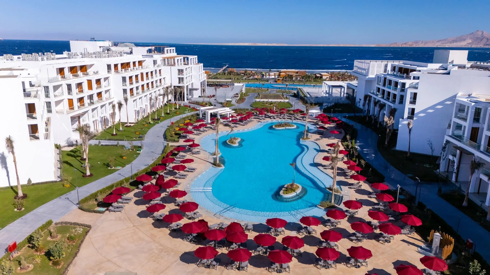 Resort fronte mare con piscina circondata da ombrelloni rossi
