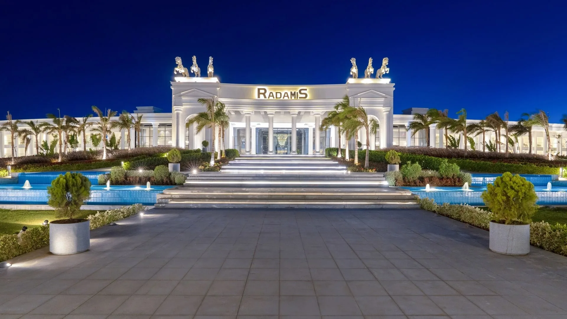 Ingresso illuminato dell'hotel Radamis con statue e fontane di notte